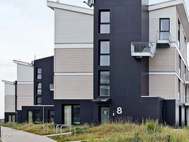 Un edificio residencial moderno de varios pisos con techo plano, ventanas amplias y un balcón visible.