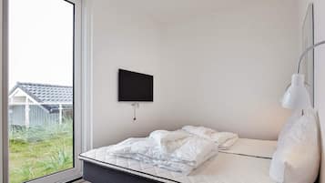 Un dormitorio con una cama, un televisor montado y una lámpara de noche.
