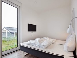 Un dormitorio con una cama, un televisor montado y una lámpara de noche.