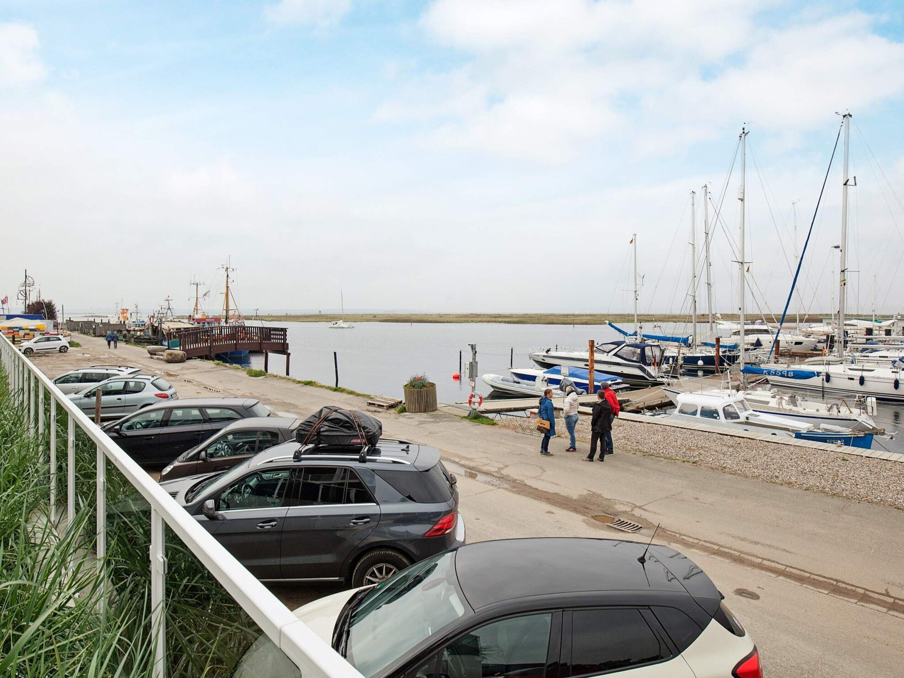 A marina with parked cars and boats, a wooden dock, and a clear view of the water.