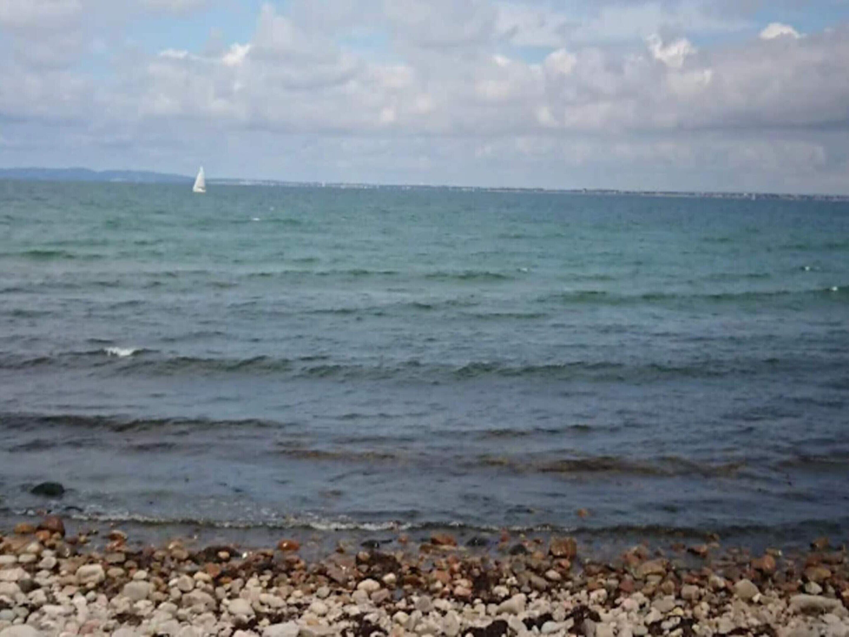 A rocky shoreline with calm sea and a distant sailboat.