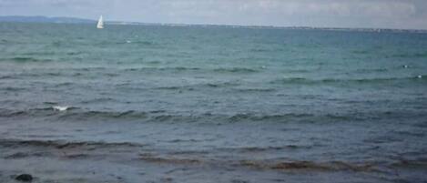 A rocky shoreline with calm sea and a distant sailboat.