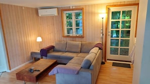 A cozy living room with a sofa, a coffee table, and a lamp. There is a window with a view of greenery outside. - 5 Person Holiday Home in Dronningmolle (Dronningmolle)