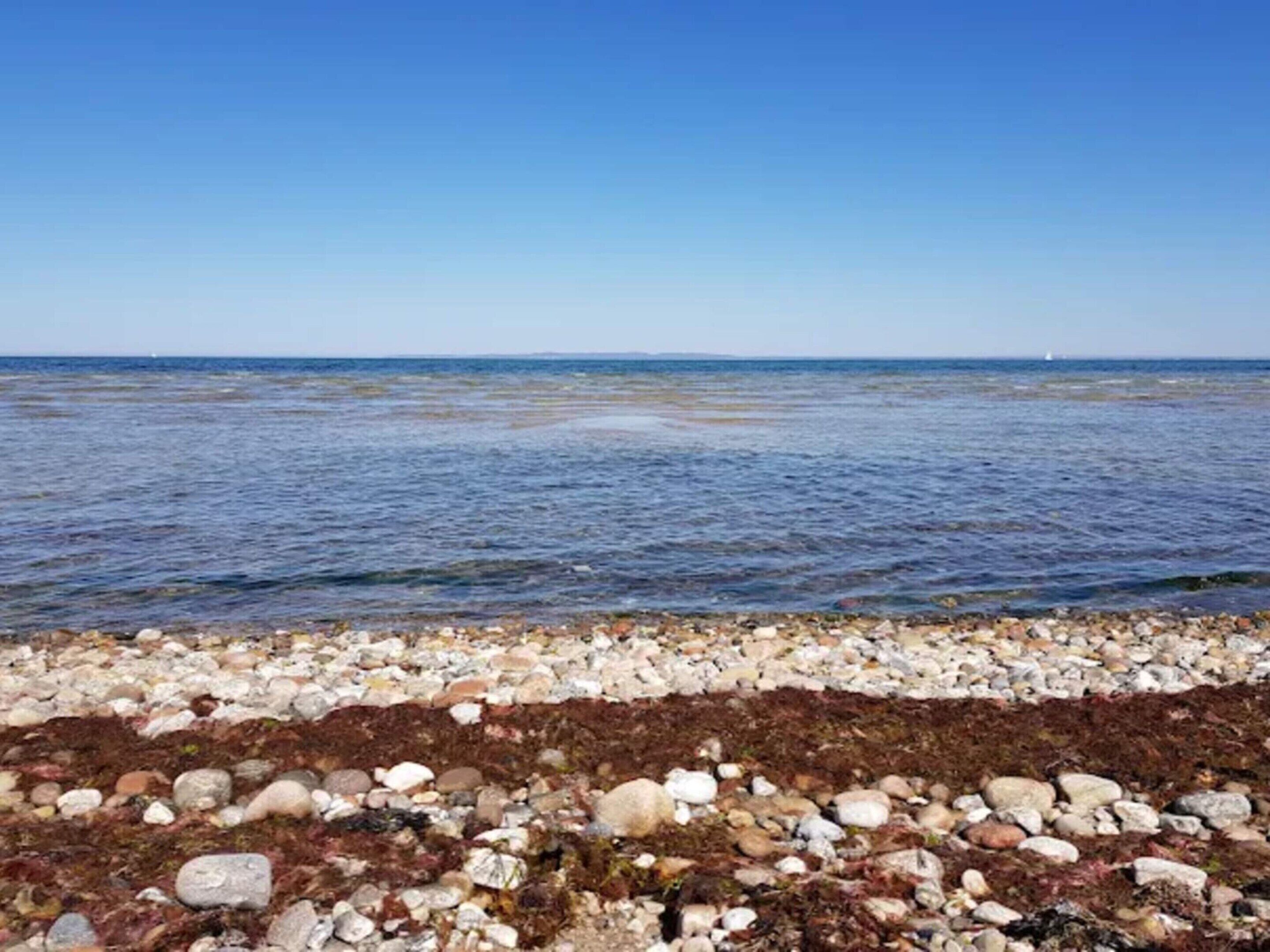 Eine felsige Küstenlinie mit klarem, blauem Wasser und einem entfernten Segelboot.