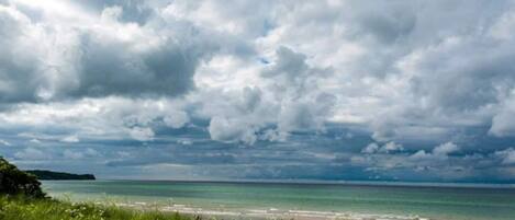 A coastal landscape with a beach, grassy foreground, and a cloudy sky.
