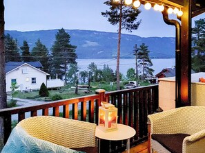 A balcony with wicker chairs and a table, overlooking a residential area with houses and a body of water. - 6 Person Holiday Home in Honefoss (Hole)