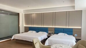 Una habitación de hotel moderna con dos camas, un separador de vidrio, una mesita de mármol y un sillón beige.