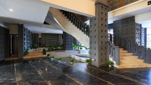 Un vestíbulo amplio con una escalera moderna, suelo de mármol y plantas en macetas.