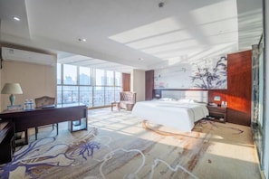 A hotel room with a large bed, a desk, a chair, and a view of the city through large windows. - Chengshi Daren Garden Hotel (Laibin)