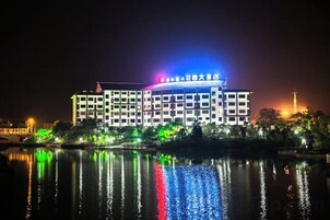 Un edificio de varios pisos con una superficie acuática reflectante en primer plano, posiblemente un hotel o centro de convenciones.