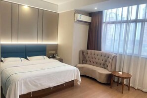 Una habitación de hotel con cama, zona de estar, una mesita y una ventana con cortinas.