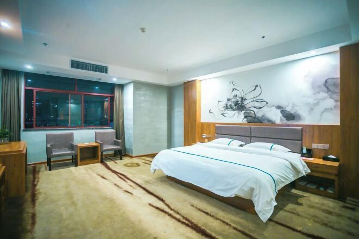 Una habitación de hotel con una cama grande, dos sillas, una mesita y una ventana con cortinas.