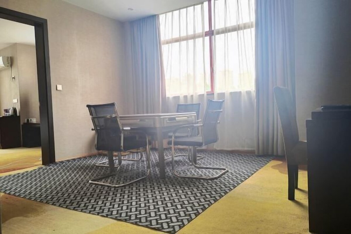 Una sala de conferencias con una mesa y sillas, una alfombra estampada y un ventanal con cortinas.
