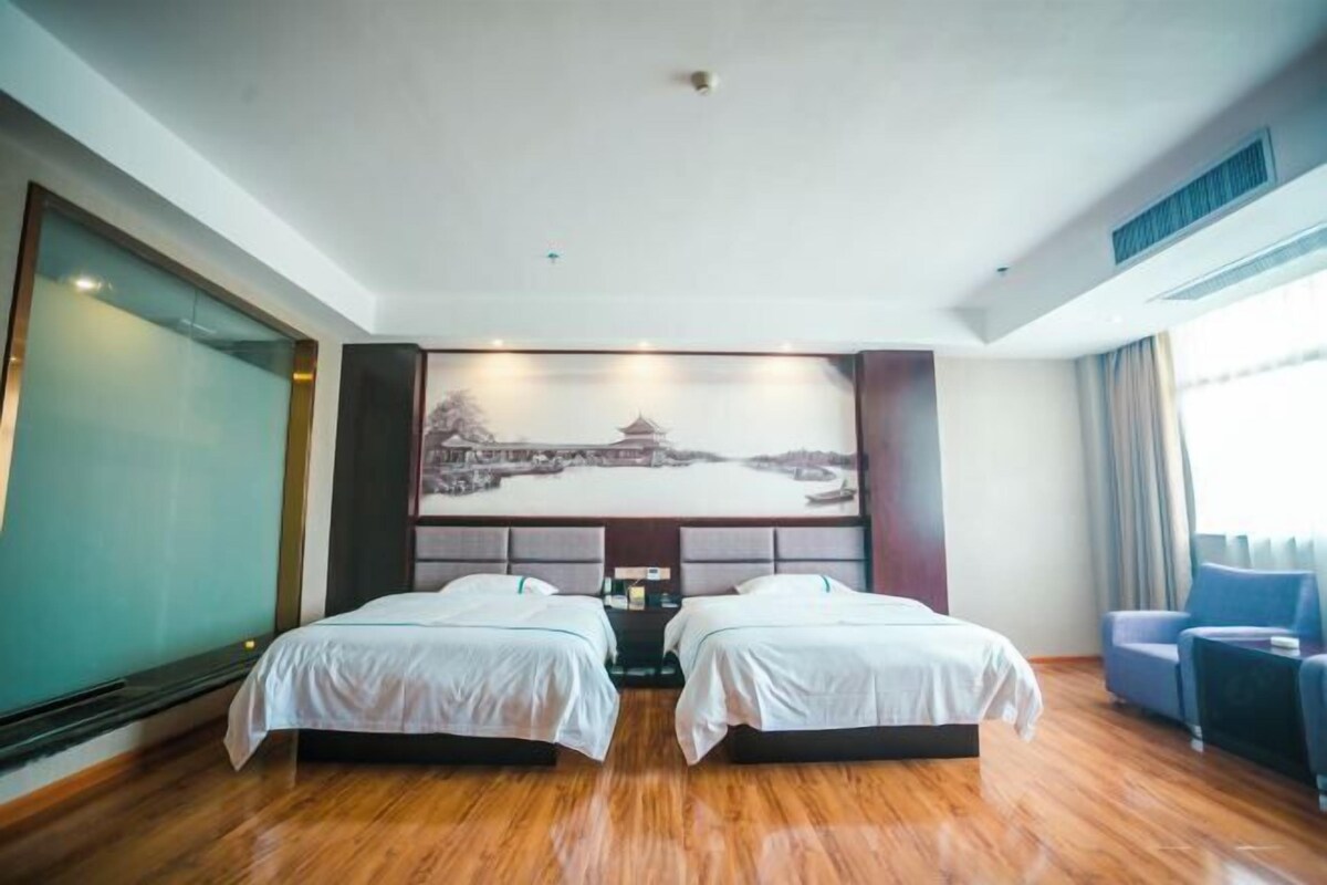Habitación de hotel con dos camas, un cuadro grande de un paisaje y vista a un cuerpo de agua.