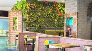 Un restaurante con sillas y mesas de colores, una pared verde con plantas y un piso azul.