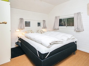 A bedroom with a bed, two windows with curtains, a bedside table, and a nightstand.