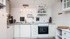 A kitchen with white cabinets, a stove, and a sink. There are hanging lights and a window above the sink. - 6 Person Holiday Home in Glesborg (Glesborg)