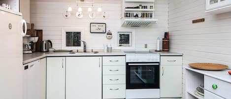 A kitchen with white cabinets, a stove, and a sink. There are hanging lights and a window above the sink.