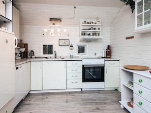 A kitchen with white cabinets, a stove, and a sink. There are hanging lights and a window above the sink.