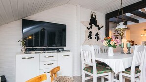 A dining area with a white table, chairs, and a television mounted on a white cabinet. - 6 Person Holiday Home in Glesborg (Glesborg)