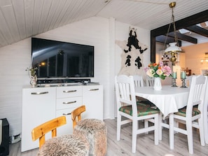 A dining area with a white table, chairs, and a television mounted on a white cabinet.