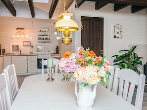 A dining table with a white vase of flowers, a candle, and a hanging light fixture.
