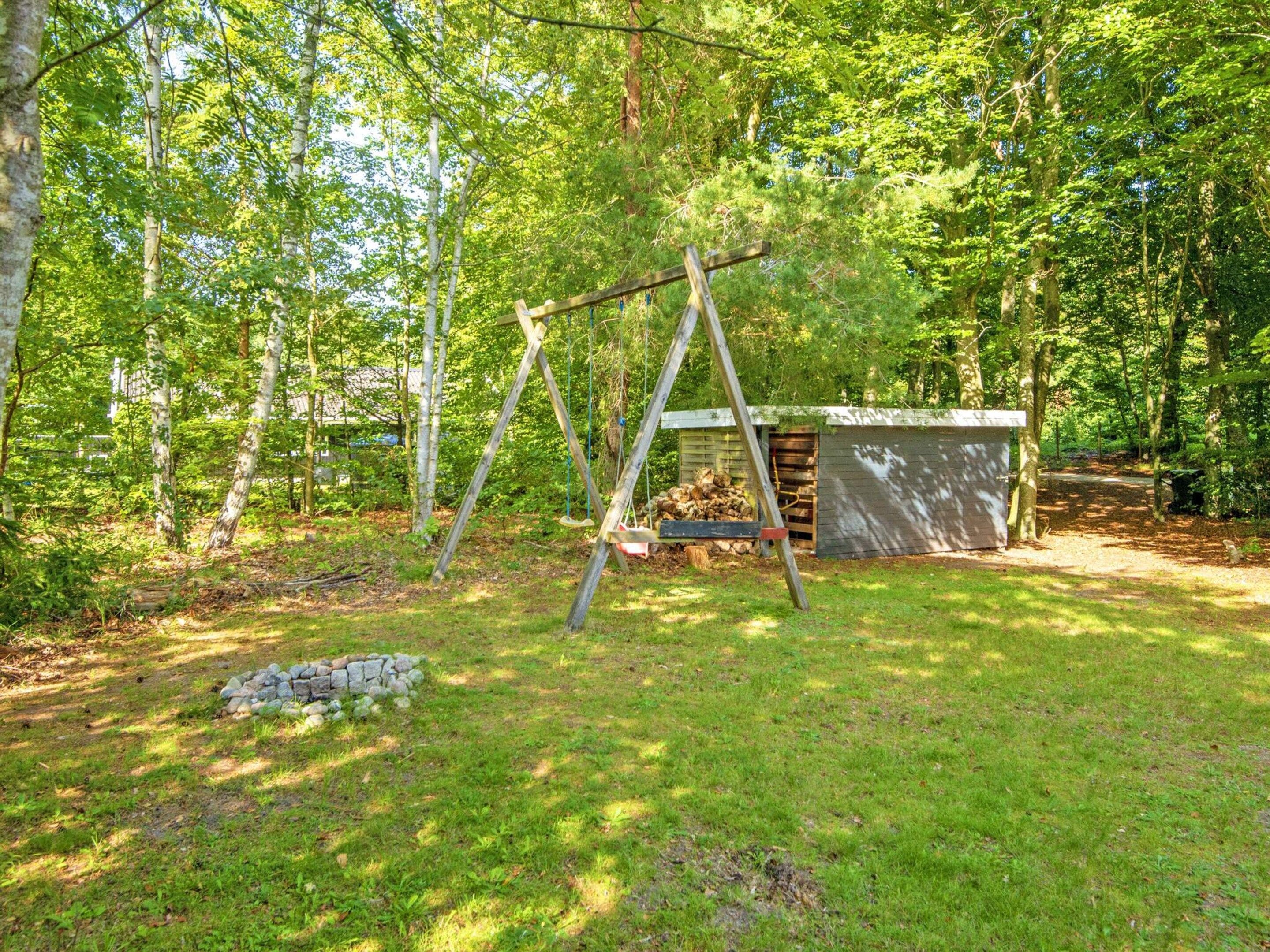 Ein hölzernes Schaukelgerüst in einem bewaldeten Gebiet mit einer kleinen Laube und einem Holzstapel.