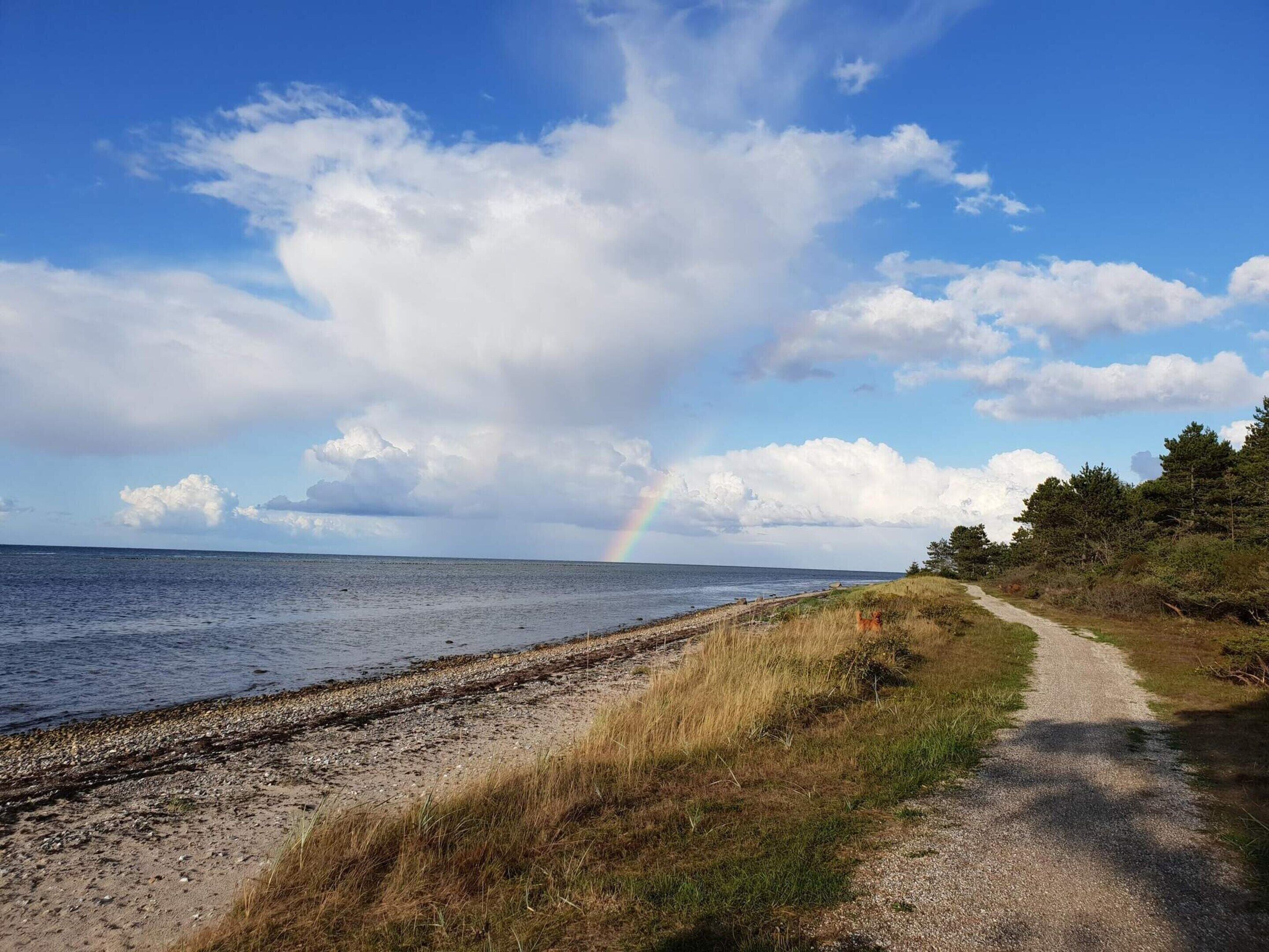 A coastal path with a beach, a rainbow, and a clear sky.
