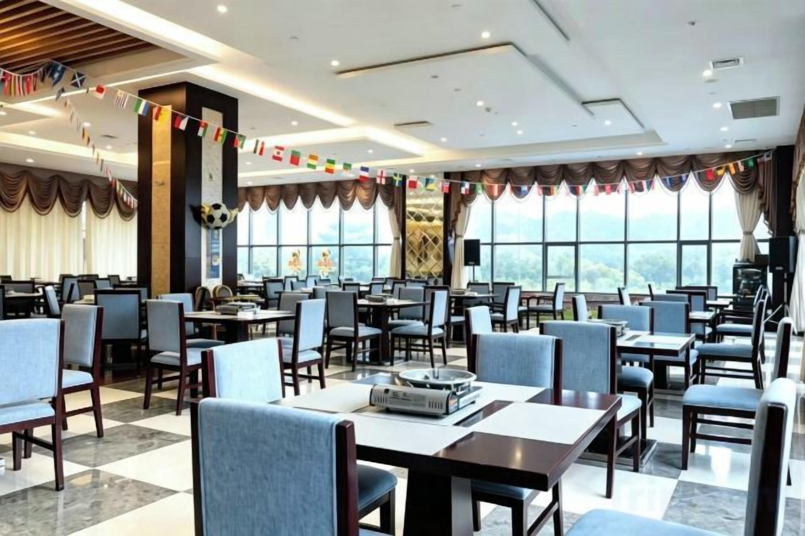 A spacious dining area with multiple tables and chairs, large windows, and a view of the outdoors.