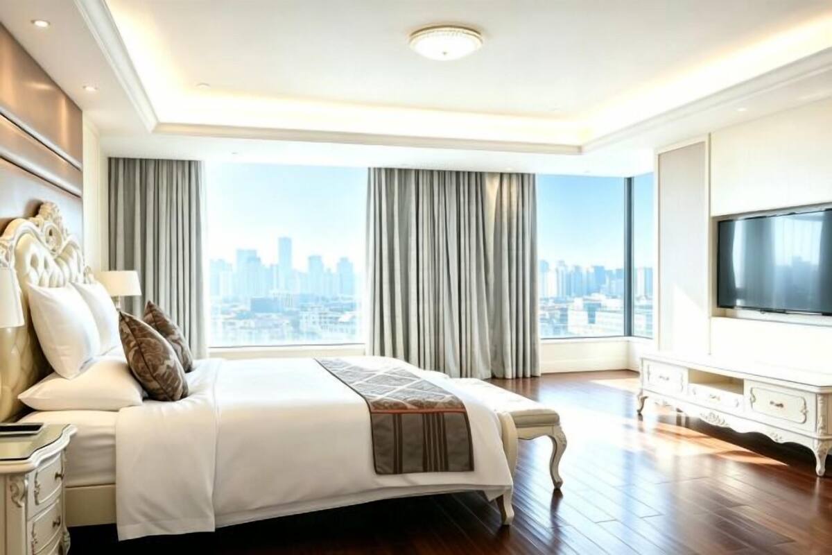 Una habitación de hotel espaciosa con una cama grande, televisión, vista a la ciudad y diseño moderno.