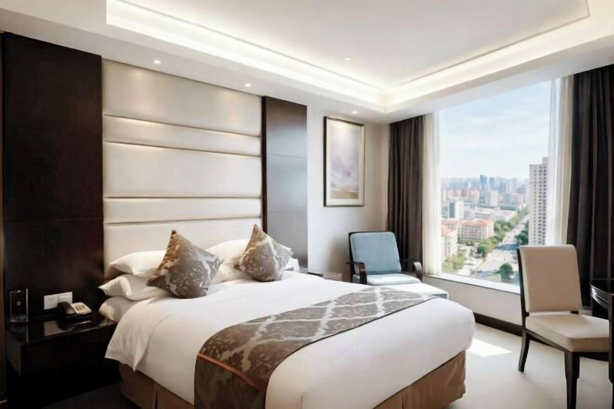 Una habitación de hotel moderna con una cama grande, vistas a la ciudad, un escritorio y una silla.