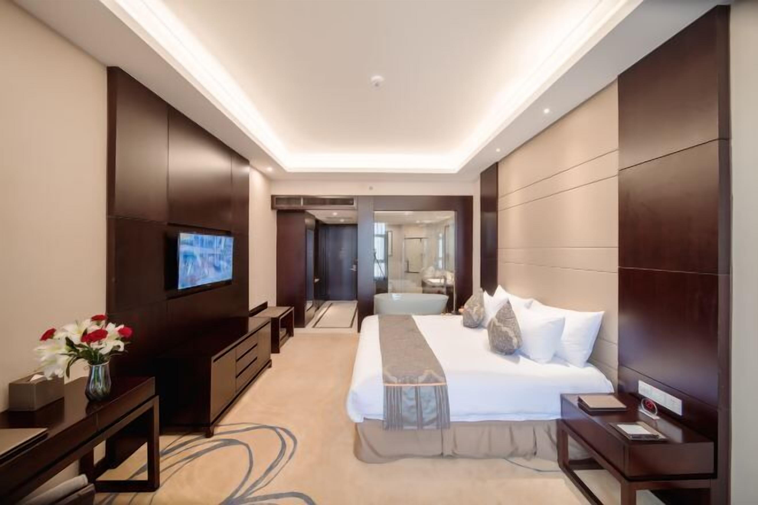 A modern hotel room with a large bed, a TV, a desk, and a comfortable seating area.