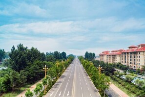 A multi-story hotel with a red roof, a wide road with directional arrows, and a green park on either side.