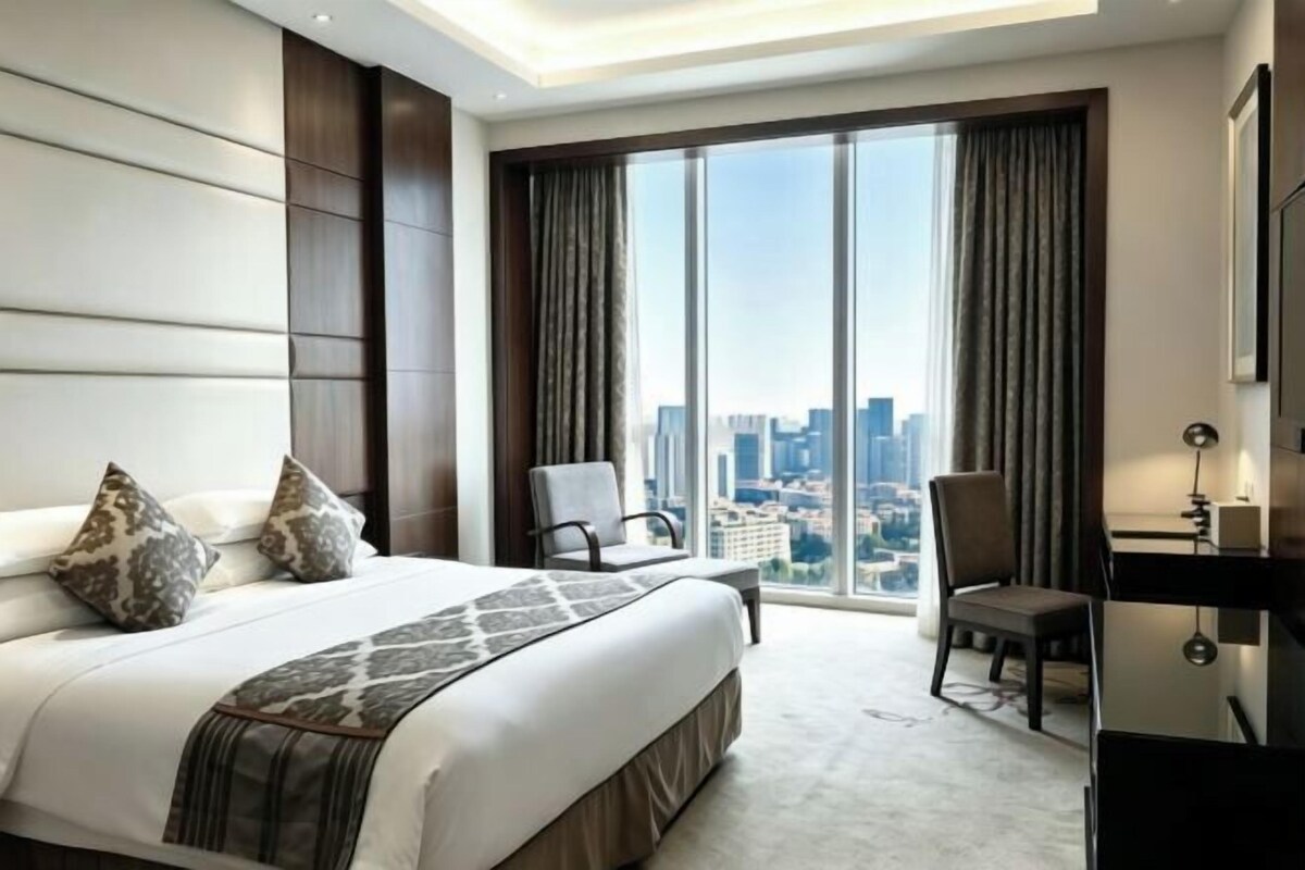 Habitación de hotel con una cama grande, dos sillas, un escritorio y vistas a la ciudad.