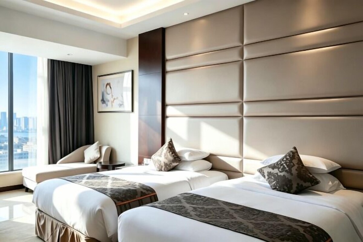 Habitación de hotel con dos camas, un sofá, vistas a la ciudad y un cabecero grande y acolchado.