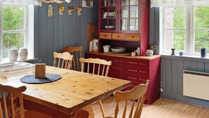 Ett matbord i trä med stolar, ett köksområde med skåp och ett fönster samt ett element.