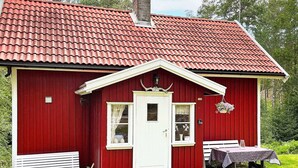 En röd träbyggnad med en vit dörr, ett litet fönster och en veranda med en bänk.