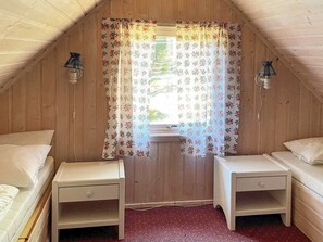 A small, cozy attic bedroom with two single beds, wooden walls, a floral curtain, and two wall-mounted lamps. - 6 Person Holiday Home in Halden (Halden)