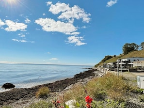 A coastal view with a rocky shoreline, a clear sky, and a building with outdoor seating. - 6 Person Holiday Home in Tomelilla (Tomelilla)