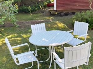 A round table with four white Adirondack chairs in a grassy outdoor area.