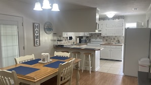 A kitchen with white cabinets, a wooden dining table with blue placemats, and a clock on the wall. - Papa & Mema’s Farmhouse (Hazlehurst)