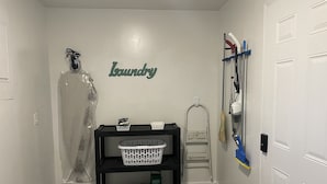 A laundry area with a wall-mounted sign reading "Laundry," a basket on a shelf, a mop, and a broom leaning against the wall. - Papa & Mema’s Farmhouse (Hazlehurst)