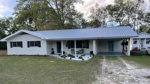 A single-story house with a covered front porch, a small front yard with a gravel path, and a brick exterior. - Papa & Mema’s Farmhouse (Hazlehurst)