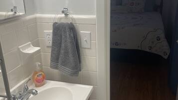 Ein Badezimmer mit einem weißen Waschbecken, einem Spiegel und einer Seifenspender. Ein Handtuch hängt an einem Haken.