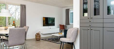 Un salon moderne comprenant un coin repas, un téléviseur à écran plat et des meubles de rangement gris.