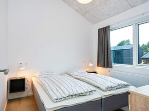 Un dormitorio con dos camas, lámparas de noche, una ventana con cortinas y vistas a un edificio.