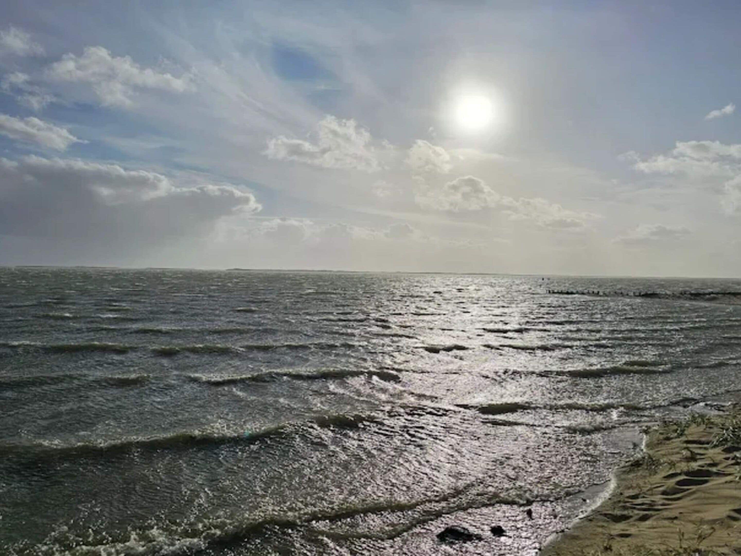 A beach with waves, a clear sky, and a sun.