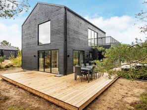 A modern two-story house with a wooden deck, large sliding glass doors, and a balcony.