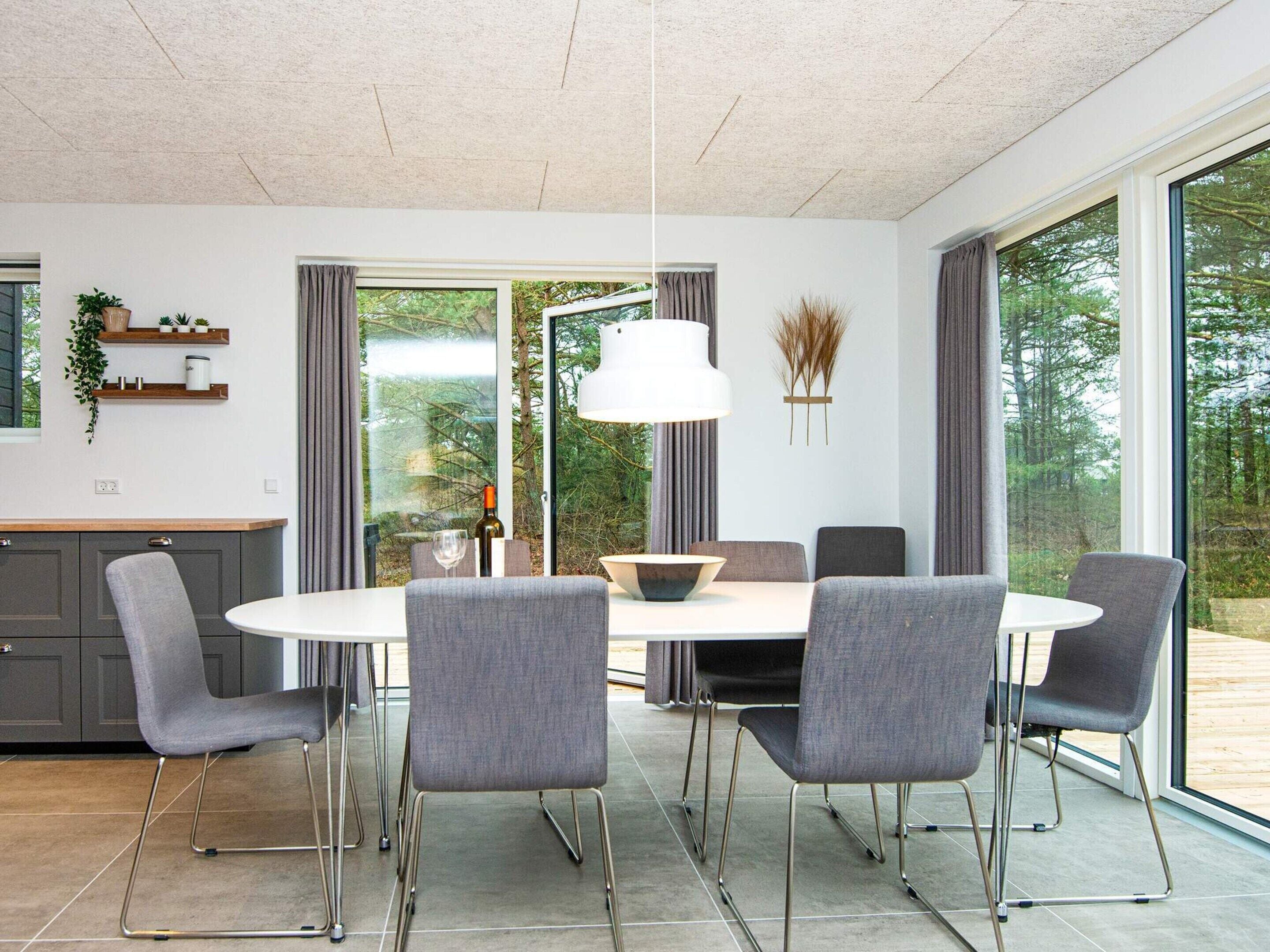 A modern dining area with a round table, grey upholstered chairs, and a pendant light.