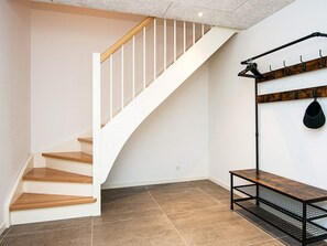 Una escalera con escalones de madera y barandillas blancas, un perchero fijado a la pared y un banco con estructura metálica.